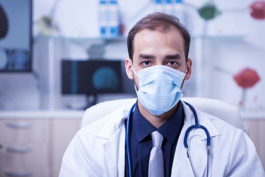Portrait of serious doctor wearing a protection mask over his mouth. Close up portrait of young doctor in his cabinet at the clinic.