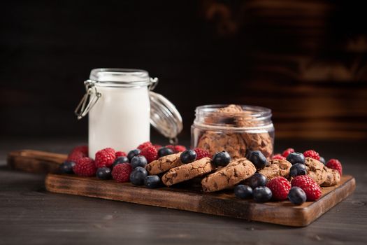 Delicious brown cookies on wooden plate with fresh bluebarries. Organic milk.