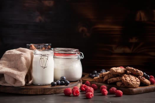 Delicious cookies with dark chocolate and blueberries over rustic wooden table. Stacked cookies with milk.