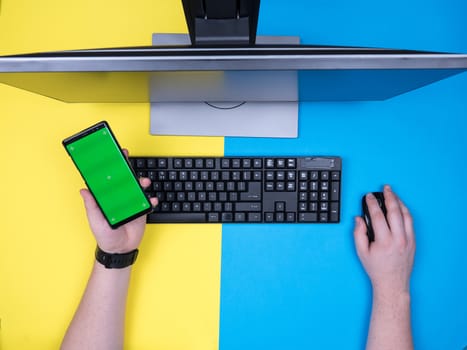 Flat lay top view of man holding a hand on his mouse and the other holding a mobile phone. Green screen on phone. Entreprenour concept.