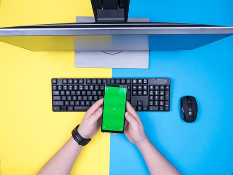 Flaty lay top view of freelancer hand's holding a modern phone. Blue background. Green screen on mobile phone.