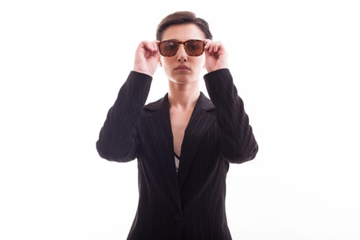 Beautiful young model posing with sunglasses and wearing a black jacket over white background in studio. Pretty model.