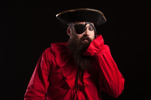 Attractive bearded man in a pirate costume for carnival touching his eye patch with his arm hook. Man in a halloween costume.