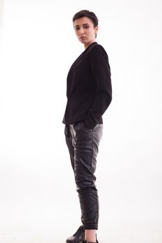Full lenght portrait of young female model with black jacket holding hands in her leather pants. Caucasian fashion model.