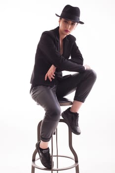 Caucasian beauty with a stylish hat sitting on a chair over white background in studio Elegant and stylish woman.