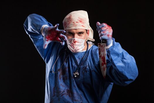 Doctor covered in blood with mask on his face for halloween in studio. Portrait of a doctor looking like a scewball.
