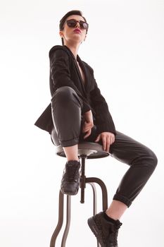 Portrait of fashion model looking down on the camera sitting on a chiar in studio over white background. Full body portrait of stylish woman.