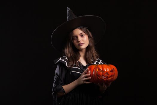 Little girl with a serious expression making a spell while holding a pumpking for halloween. Child dressed up for halloween carnaval.