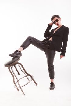 Brunette fashion model posing in studio with one leg up on a chair over white background. Stylish jacket.