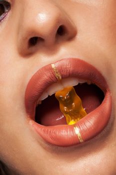 Close up view of beautiful woman lips with gummy bear. Concept shot. Studio shot. Beauty shot. Fashion shot.