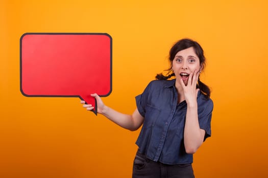 Shocked young woman with a speech bubble against a yellow background in studio. Surprised woman with thought bubble.
