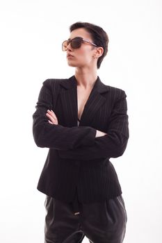 Attractive fashion model posing in black jacket wearing sunglasses over white background in studio. Model in her 20s.