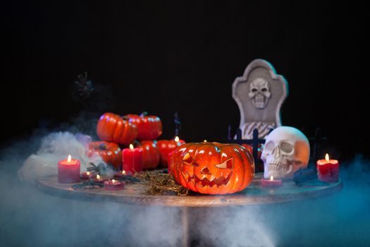 Scary pumpkin and creepy skull sitting together on a wooden table at halloween party. Halloween smoke. Haunted headstone.
