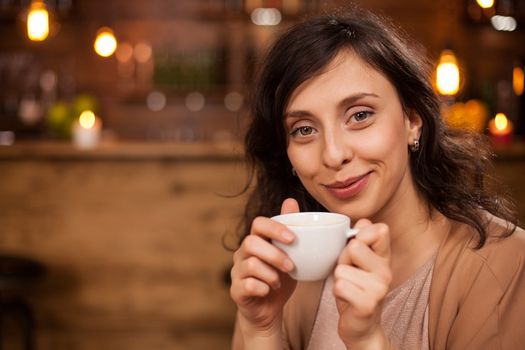 Attractive caucasian woman smilling and looking at the camera with a coffee cup in hand. Woman relaxing in a coffee shop. Woman enjoying a good coffee.