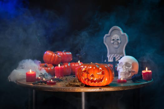 Wooden table with different halloween decorations. Creepy halloween pumpkin. Burning candles.
