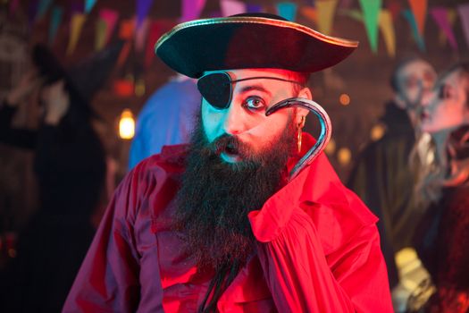 Portrait of funny man in a pirate costume playing with his hand hook at halloween celebration. Cheerful pirate.