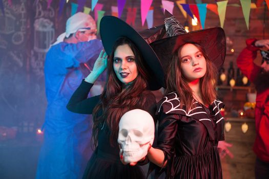 Two witches at a halloween celebrating holding a human skull. Cheerful witches. Looking at the camera.