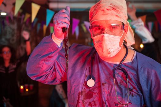 Scary doctor holding a knife with blood on it at halloween celebration party. Halloween costume.