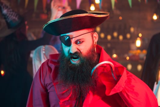 Portrait of handsome bearded man screaming and dressed up like a pirate at halloween celebration. Witch in the background.