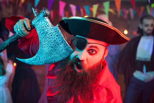 Portrait of cheerful bearded men dressed up like a pirate at a halloween party. Man in a dracula costume in the background.