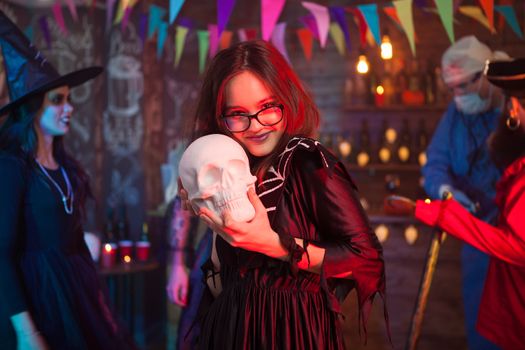 Cheerful and beautiful girl holding a human skull for halloween celebration. Girl in witch costume.