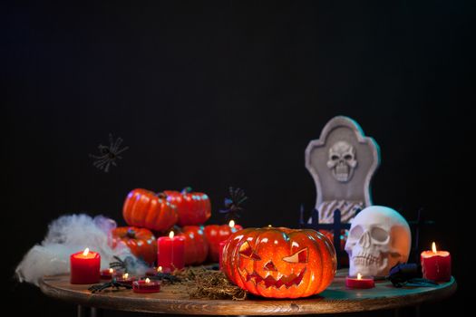 Carved scary pumpking sitting on a wooden table with a creepy skull at halloween celebration. Halloween decoration.