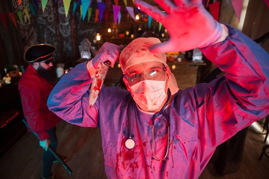 Halloween party with men dressed up like scary monsters. Creepy doctor. Scary pirate in the background.