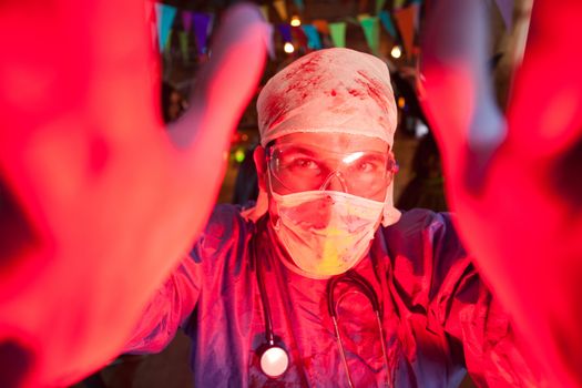 Cheerful young man dressed up like a creepy doctor for halloween. Doctor covered in blood.