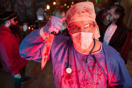 Attractive young man in a doctor costume holding a knife at halloween party. Halloween night life.