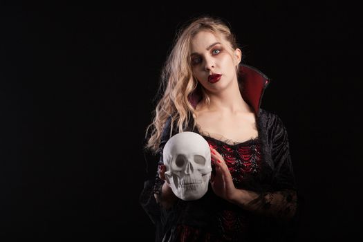 Human skeleton holded by beautiful woman dressed up like a sexy vampire for halloween. Halloween makeup.
