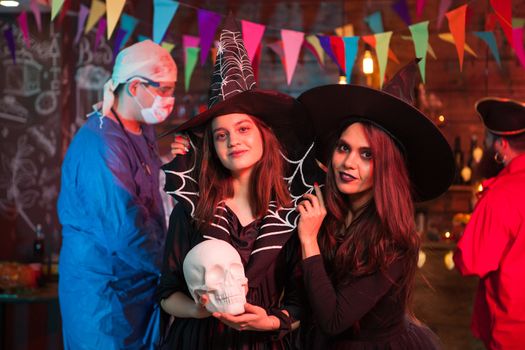 Crazy doctor with blood behind two beautiful witches at halloween party. Halloween tradition.