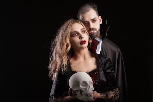 Portrait of vampire couple posing for halloween against a black background. Handsome man in Dracula costume. Seductive vampire female.