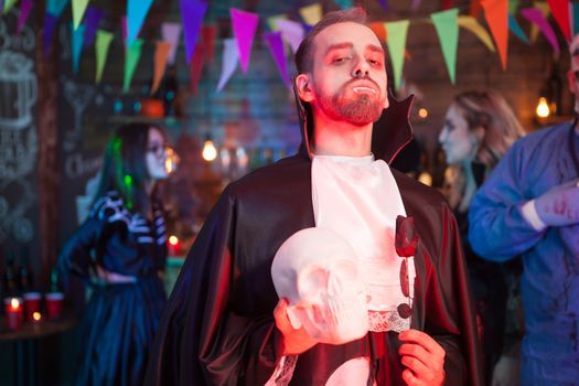 Young man dressed as vampire at Halloween party. He is holding a skeleton in hands