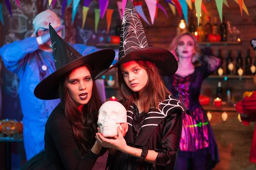 Witches with serious face holding a human skull at halloween celebration. Young witches celebrating halloween.