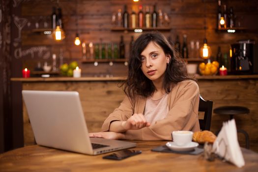 Attractive caucasian woman using her laptop in a coffee shop with interent connection. Cup of coffe. Young female entrepreneur working on her laptop in a coffee shop. Entrepreneur lifestyle.