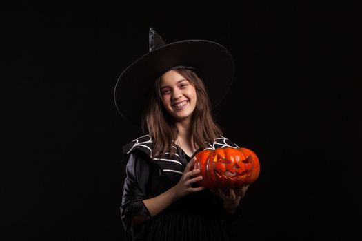 Little girl in a witch costume doing witchcraft on a scary pumpkin. Happy child in a witch costume for halloween.