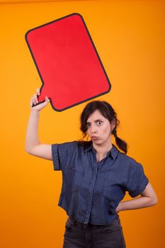 Portrait of discontent young woman holding an empty thought bubble in studio over yellow background. Copy space available. Woman holding empty placard.