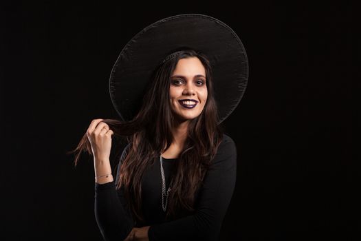 Cheerful beautiful woman in a witch costume with scary make up for halloween. Girl in black dress for halloween.