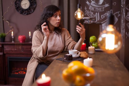 Young pretty woman using mobile phone in a coffee shop and making funny faces. Hipster young woman in a coffee shop.