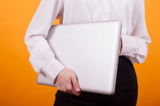 Portrait of young girl holding a laptop in studio over yellow background. Teen girl holding a laptop.