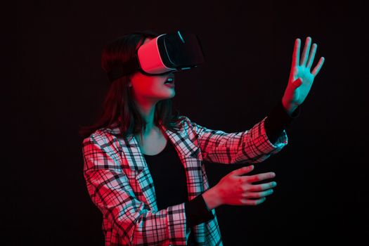 Young girl wearing virtual reality goggles headset in studio with colorful lighting. Futuristic virtual reality goggles.