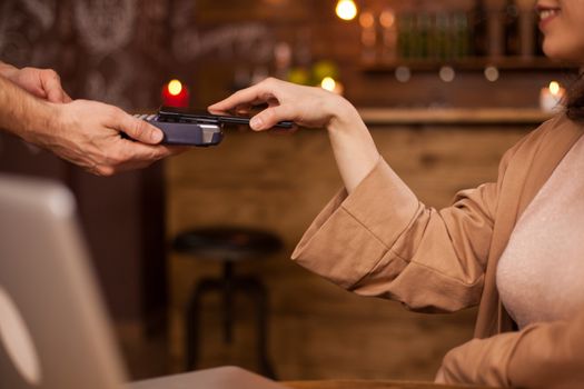 Hand of customer paying with contactless mobile phone technology in a coffee shop. Woman paying with mobile phone for her coffee. Commercial activity in a coffee shop.