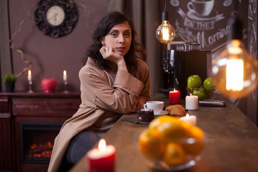 Portrait of beautiful young woman looking at camera and sitting at the bar counter in a elengat coffee shop. Gorgeous caucasian young woman in a coffee shop.