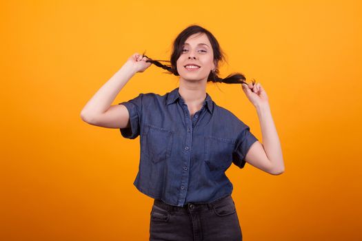 Happy young woman happy about her shampoo for her demaged hair in studio over yellow background. Beautiful girl with cute smile.
