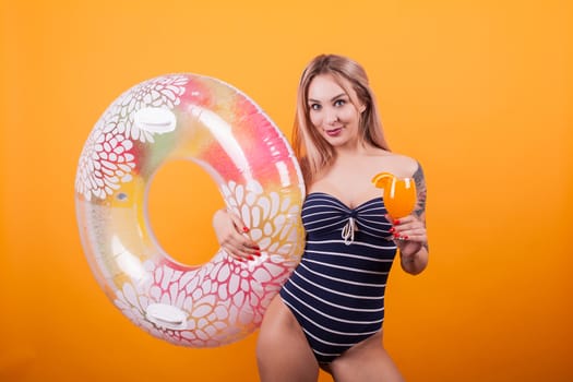 Happy young woman in swimming suit holding summer cocktail over yellow background. Holding swim ring. Attractive woman. Cheerful woman.