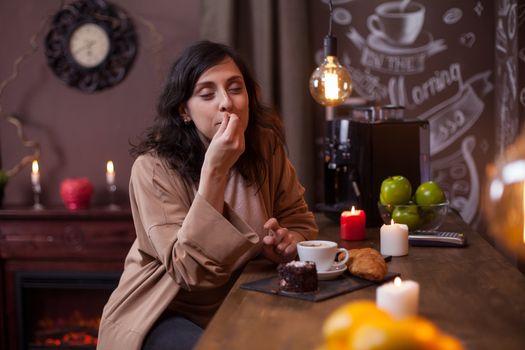 Portrait of cute young woman enjoying a tasty cake in a coffee shop at bar counter. Cheerful young woman eating cake in a hipster coffee bar.