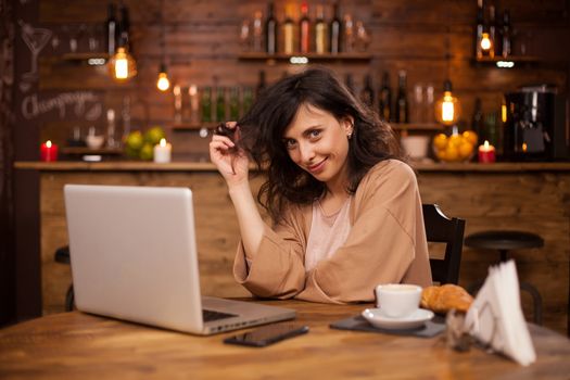 Portrait of caucasian woman smiling at the camera in a hispter coffee shop. Young female antrepenur working on laptop in a coffee shop. Coffee shop with wireless connection.