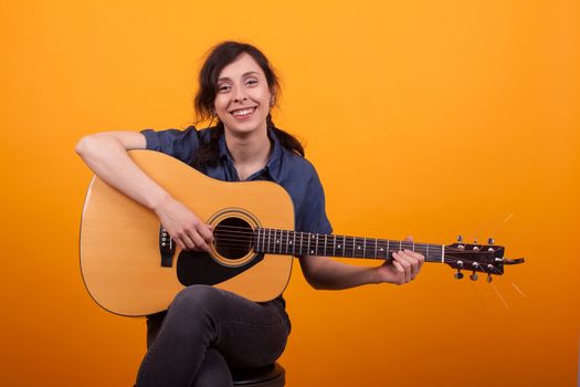 Portrait of beautiful young woman smiling in studio with guitar over yellow background. Pretty young musician woman. Young female artist. Cheerful woman with musical instrument.