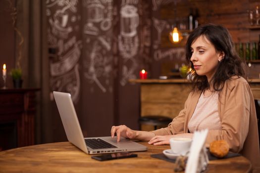 Side view portrait of young female blogger writing her aticle on a coffee shop using her laptop. Young Female entrepreneur doing business on her laptop. Coffee shop with internet connection.