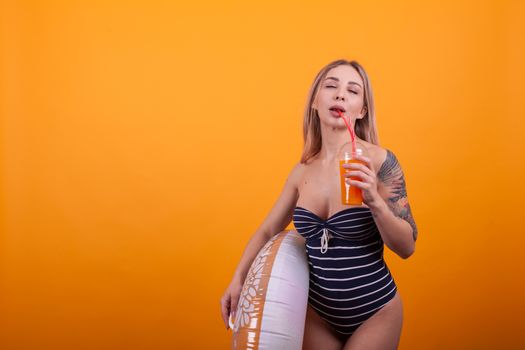Attractive girl with perfect body in swimming suit and holding a swimming ring in studio over yellow background. Stylish woman in luxury swimming suit. Sexy beautiful woman in swimming suit.